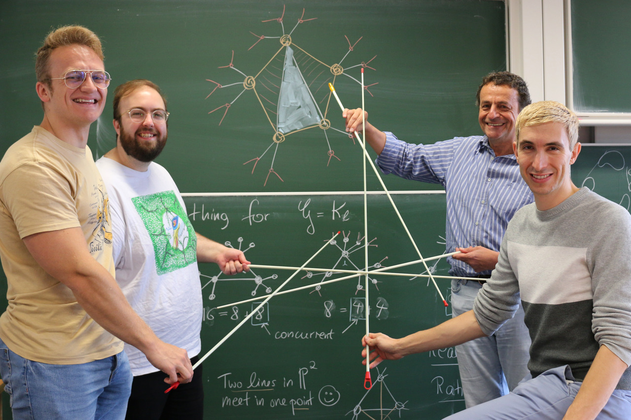Researchers illustrating configurations of lines in front of a blackboard.